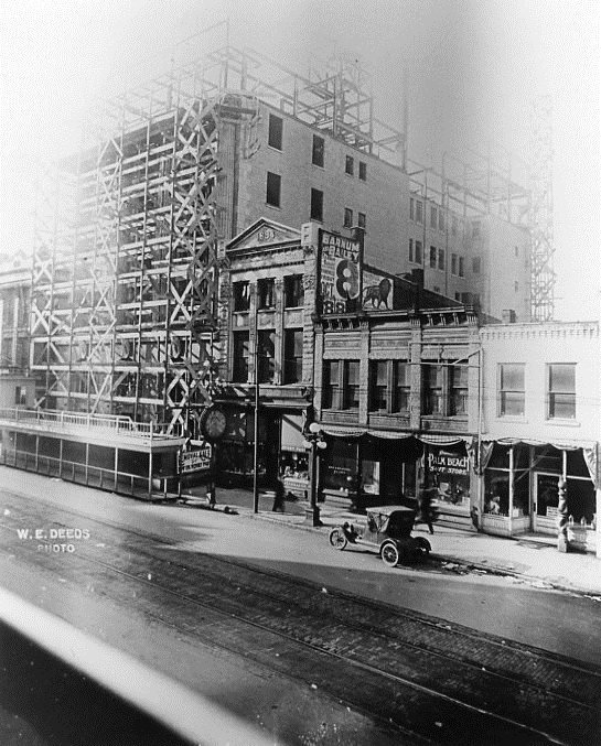 Black and white photo: vintage street scene with cars, buildings, and scaffolding.