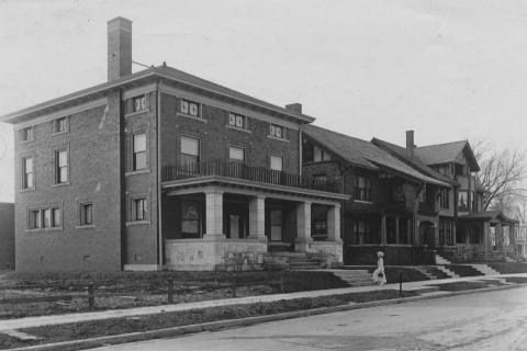 Vintage photo of brick houses with porches and a person walking by.
