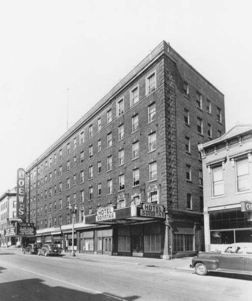 A vintage street scene with the Hotel Sonntag building, a theater marquee, classic cars, and adjacent businesses.