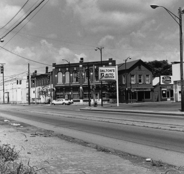 A black and white photo of an old street with buildings, signs for Dalton's Auto Service and Kibby Cleaners, and a vintage car.