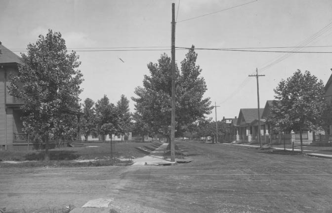 A vintage photo showing a tree-lined residential street with houses and utility poles.