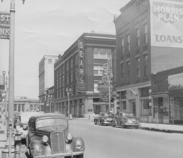 Vintage street scene with old cars and a Sears store.