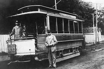 Historic streetcar with two men, one standing by the car and the other on the platform. Vintage setting.