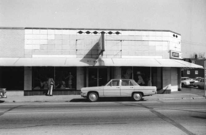 Vintage street view with a classic car in front of an old storefront.