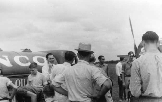 Group of people gathered around an airplane with "NC96..." on its side, under a cloudy sky.