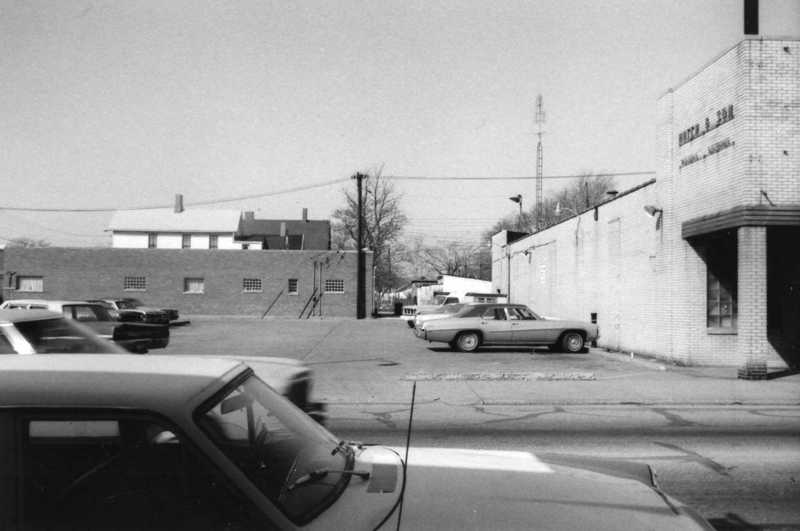 Black-and-white photo showing cars, buildings, and a clear sky.
