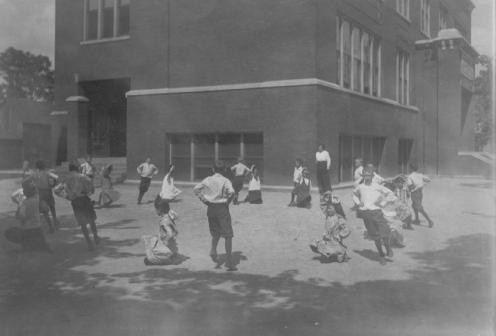 Vintage photo of children playing in a schoolyard, with a building in the background.