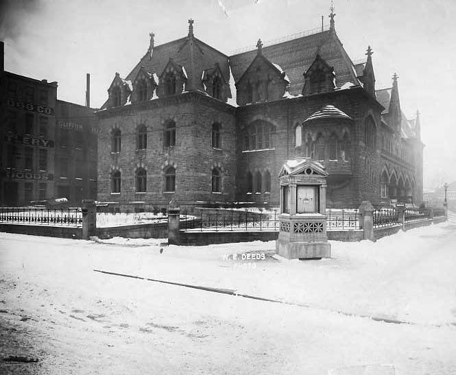 Historic building in a snowy setting with gothic architecture, next to a kiosk labeled "W.A. Deeds."