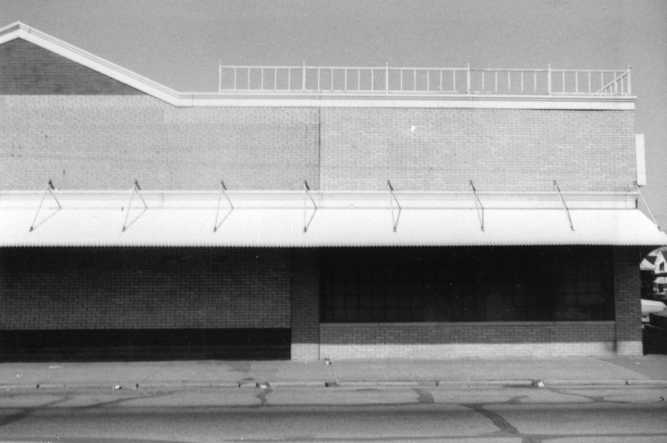 A monochrome photo of a building with an awning and brick facade, no visible windows, under a clear sky.