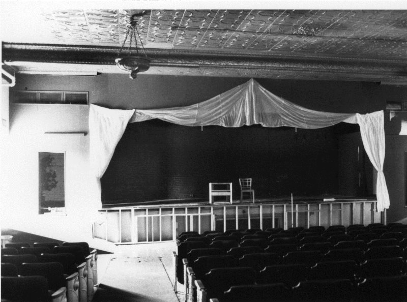 Old auditorium with stage, curtains, seats, and ornate ceiling.