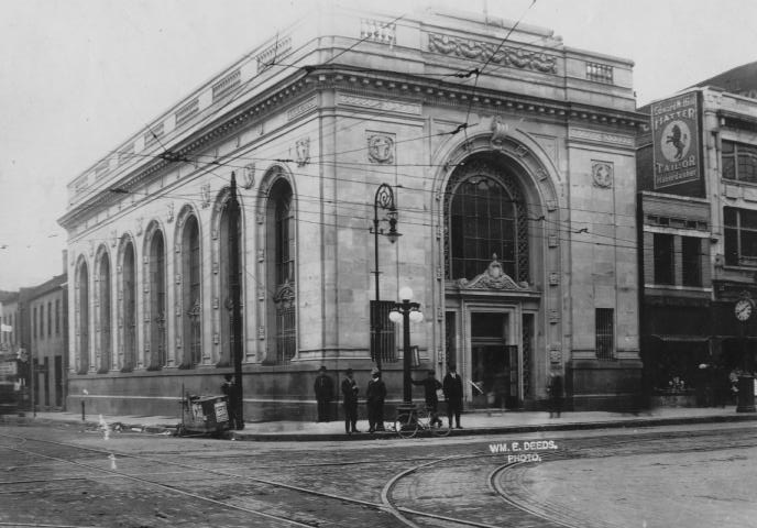 Historic building on a street corner with people outside, tram tracks in the foreground, and vintage signage.