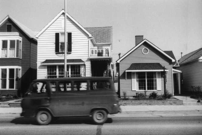 Black and white photo of suburban houses with a van driving by.