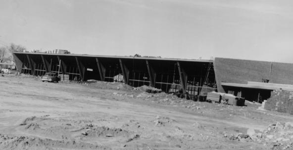 Construction site with skeletal structure of a building and scattered materials under a clear sky.
