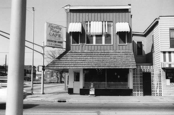Black and white photo of a quaint two-story café building with an awning and a sign reading "Knotty Pine Café."