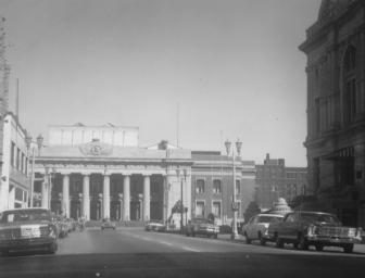 Vintage photo of a city street with classic cars and buildings with columns.