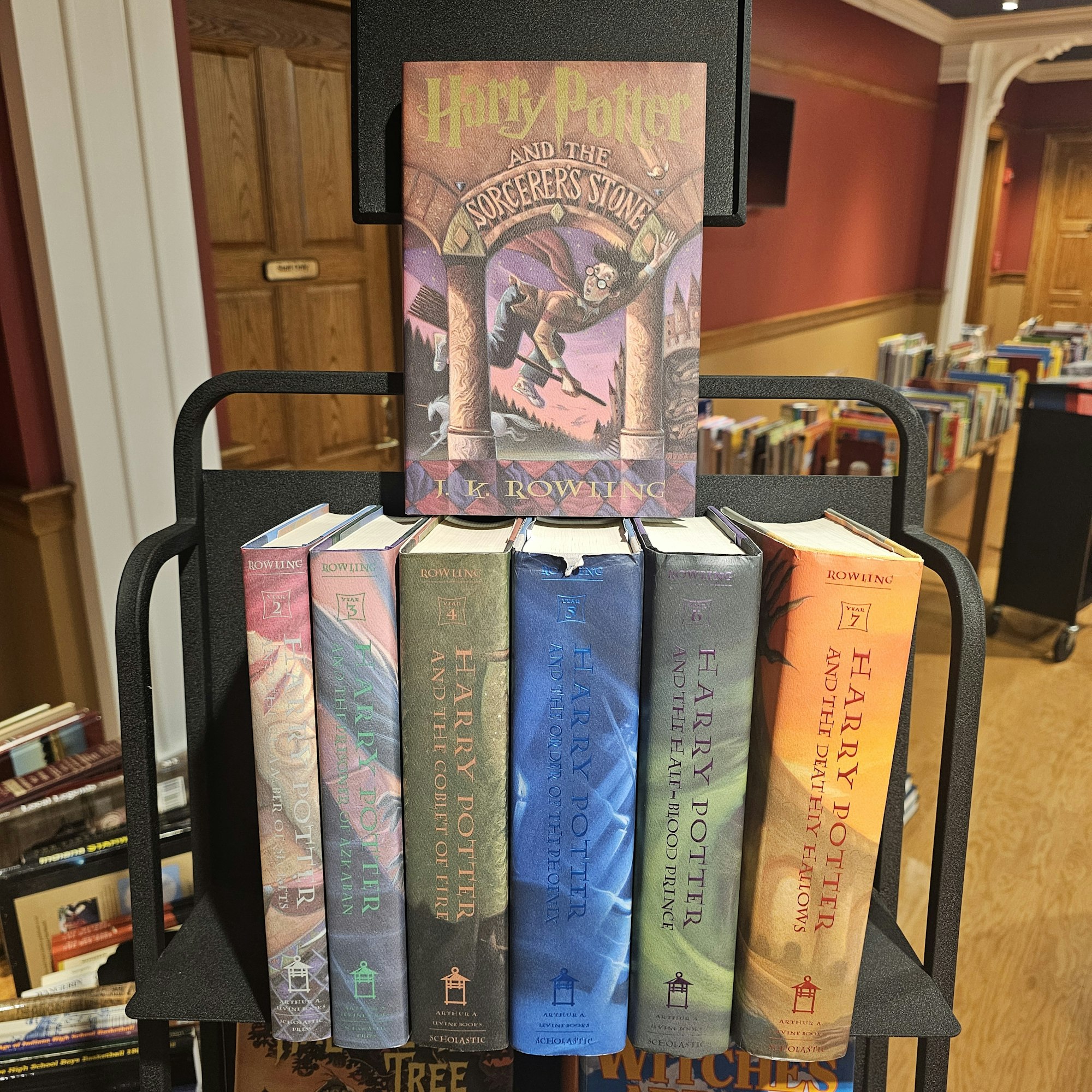 A stack of Harry Potter books on a shelf, with library in the background. Image is upside down.