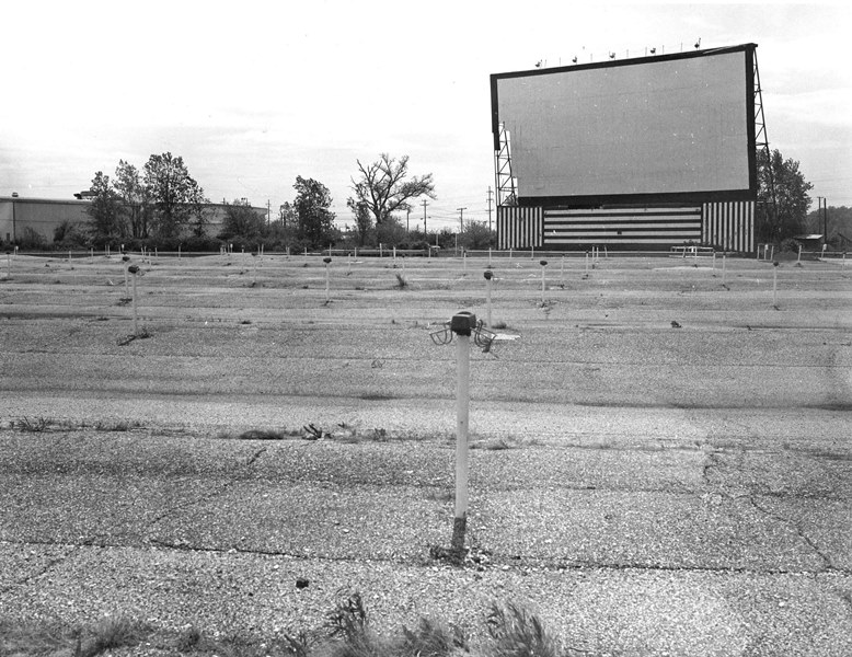 Abandoned drive-in theater with empty parking spaces and large, vacant screen.