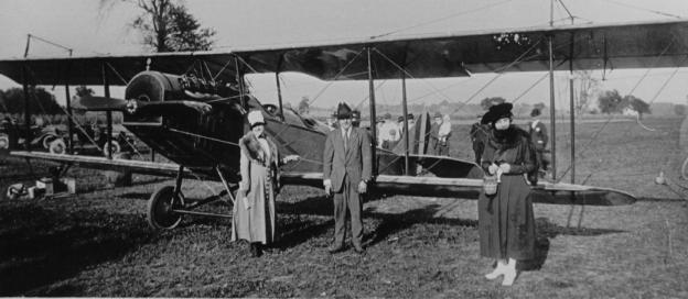 Vintage photo of three people in front of an old biplane outdoors.