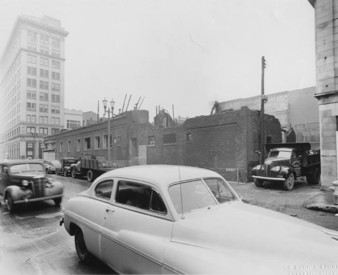 Vintage city scene with old cars, building ruins, and a tall structure in the background.