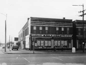 Black and white photo of an old street corner with buildings and a vintage car.