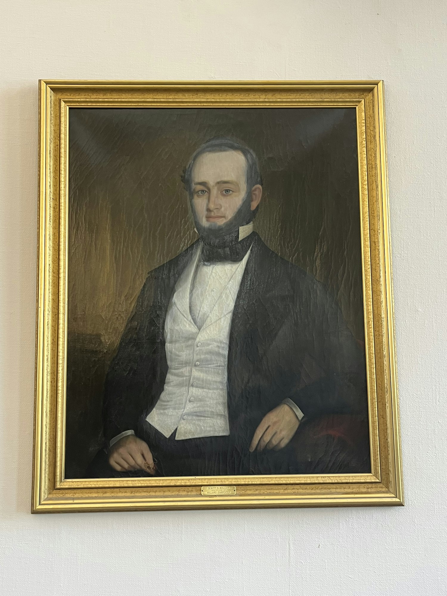 A framed painting of a man in formal attire with a beard, wearing a black suit and white waistcoat, against a dark background.