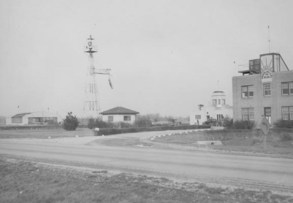 A vintage black and white photo of an old airport building with a control tower.
