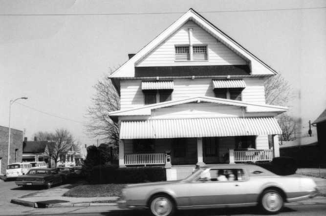 A two-story house with a porch and a car passing by in front.