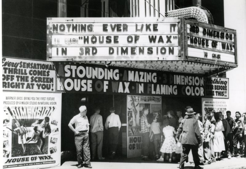 A crowd gathers outside a cinema advertising the 3D movie "House of Wax" in bold, eye-catching signs.