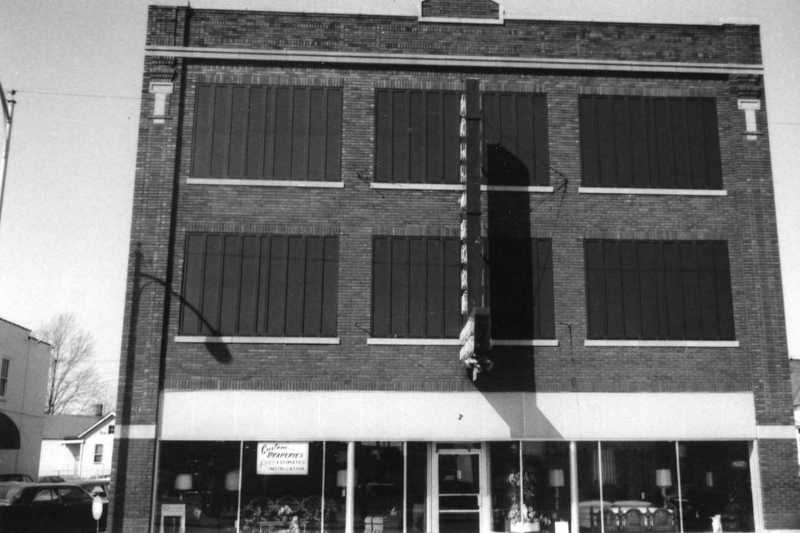 Black and white photo of a two-story building with boarded-up windows and a ladder extending to the roof.