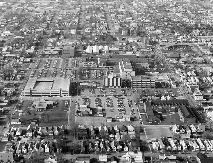 Aerial view of an urban area with dense housing, large buildings, and parking lots. Black and white photo.