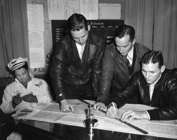 Four men in vintage attire analyze a map on a desk, with aviation-related elements suggesting a planning session.