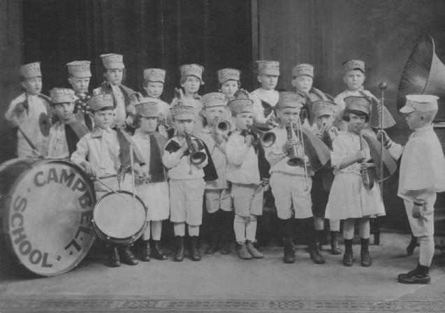 Historic photo of a children's brass band in uniform, with various instruments, and large bass drum labeled "CAMPBELL SCHOOL".