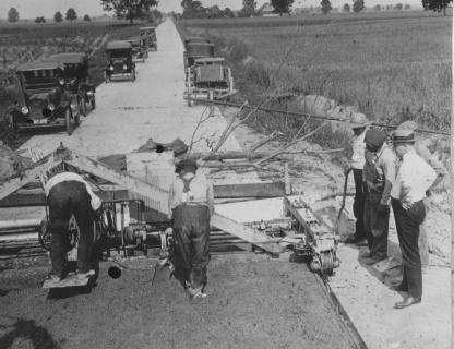 Vintage road construction with workers, old cars, and machinery.