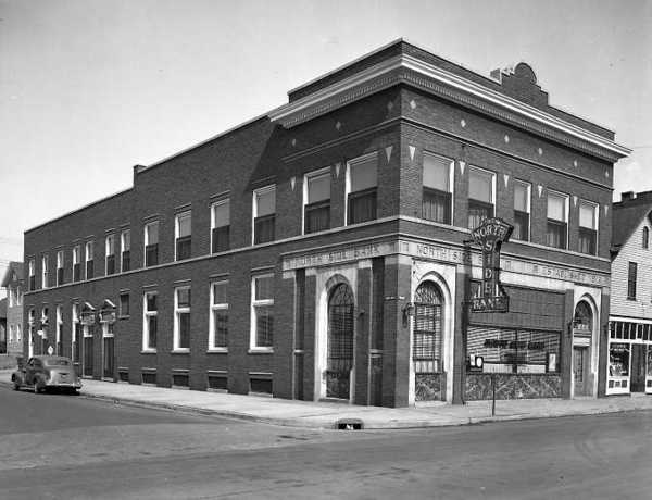 Black-and-white photo of a vintage brick corner building with arched windows and signage, possibly mid-20th century.