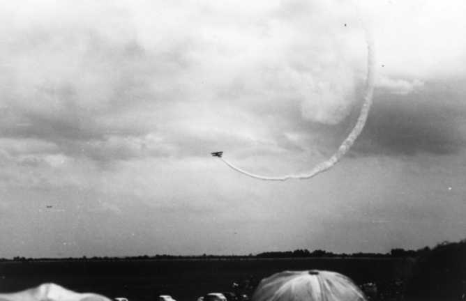 A plane flying through a cloud, creating a visible circular trail, with observers in the foreground.