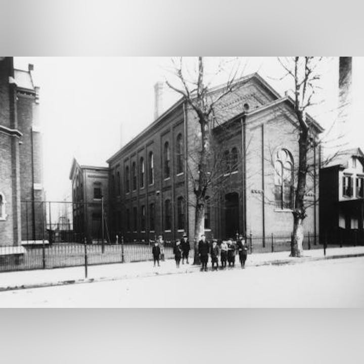 Black and white photo of a historical building with people outside, possibly from the early 20th century.