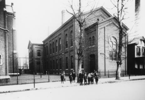 Black and white photo of a historical building with people outside, possibly from the early 20th century.