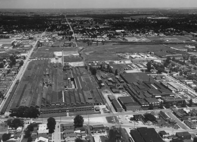 Aerial view of an industrial area with buildings next to a street, extending into a residential area, with clear skies above.