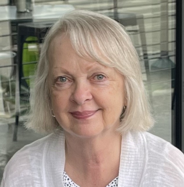 A smiling woman with short blonde hair and a white cardigan.