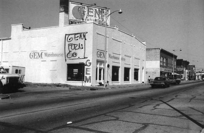 A black and white photo of an urban street with buildings, including one with "GEM Warehouse" signage.