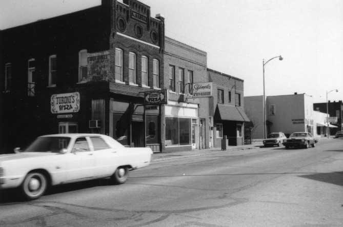 Vintage street scene with old cars and storefronts, including a pizza place.
