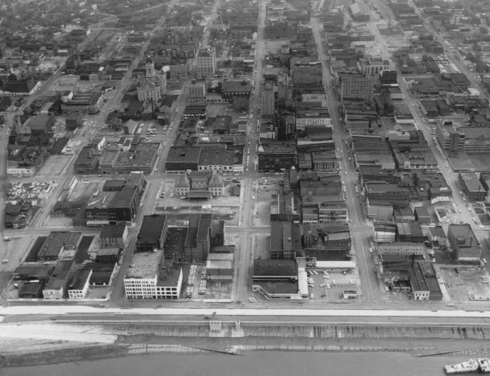 Aerial view of an urban area with grid streets, buildings of various sizes, and a waterfront.