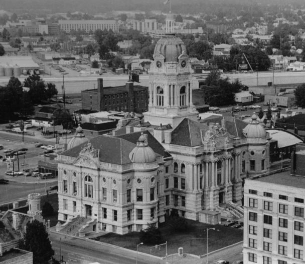 Aerial view of a grand historic courthouse with domes, surrounded by streets and buildings. Black and white photo.