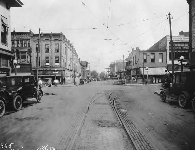 Vintage street scene with tram tracks, old cars, and buildings.