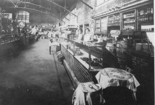 Vintage photo of an old-fashioned interior with a bar counter, staff posed, and shelves stocked with bottles.