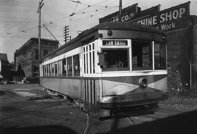 Vintage streetcar on tracks, with overhead wires, city background, signage visible.