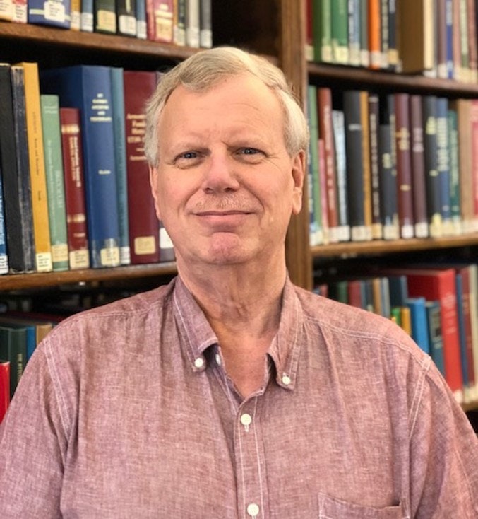 A person in a red shirt standing in front of bookshelves filled with various books.