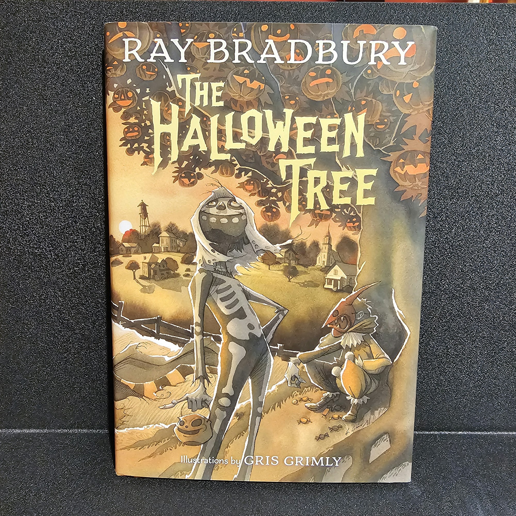 Book cover titled "The Halloween Tree" by Ray Bradbury, featuring stylized illustrations, likely Halloween-themed.