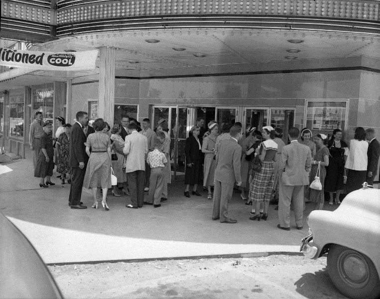 People lining up outside a vintage "Air Conditioned" movie theater.