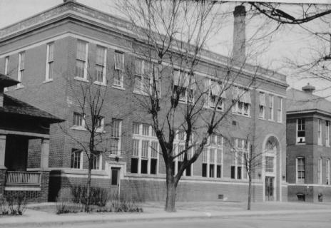 A black and white photo of an old brick building with trees in front.